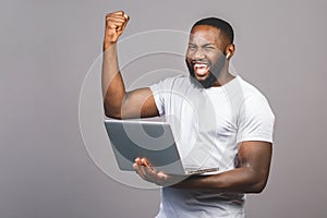 Excited happy afro american man looking at laptop computer screen and celebrating the win isolated over grey background