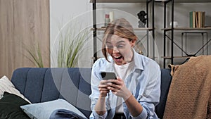 Excited happy business woman enjoy success on mobile phone at home on sofa.