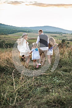 Excited happy Cauasian family enjoy while running in green summer field at sunset. Pretty young mother woman turning photo