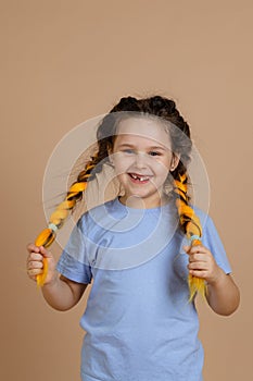 Excited happy cheerful little girl smiling with missing tooth looking at camera holding kanekalon braids with hands on