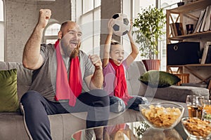 Excited, happy daughter and father watch football, soccer match together on the couch at home