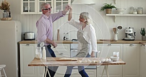 Excited happy mature couple dancing to music at kitchen table