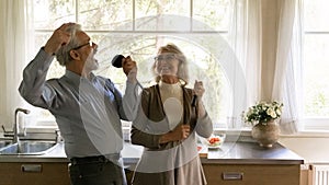 Excited happy mature family couple singing at utensils