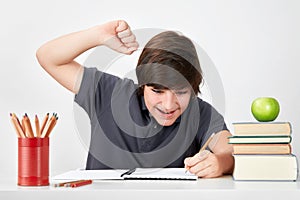 Excited and happy school boy raises his fist as a sign of glory while solving the homework question.