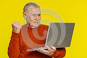 Excited happy senior man working on laptop winning lottery game, celebrating success, victory