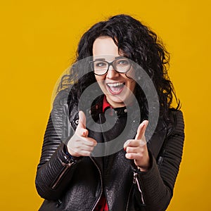 Excited happy woman in eyeglasses. Woman pointing fingers at camera, isolated on yellow. Close up portrait of hipster in glasses.