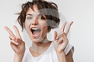 Excited happy woman posing isolated over white wall background showing peace gesture