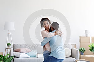 Excited happy young black couple celebrating buying new home, husband lifting wife, in moving day