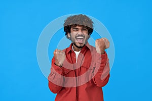 Excited happy young indian man winner showing yes isolated on blue background.