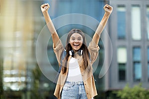 Excited happy young lady student rasising hands up outdoor