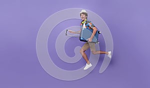 Excited happy young man tourist with luggage jumping  on purple studio background