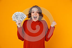 Excited happy young pretty woman posing isolated over yellow wall background holding money