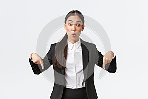 Excited and impressed asian female broker pointing fingers down, showing big deal. Astounded businesswoman discuss price
