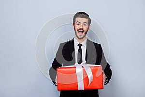 Excited and impressed man in black suit holding big red gift box