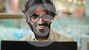 Excited Indian bearded business man in glasses reading great news on laptop celebrate online winning victory. Arabian