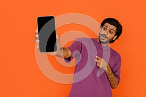 Excited indian guy pointing at smartphone in his hand