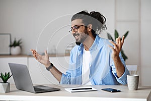Excited indian man emotionally celebrating business success with laptop computer in office