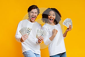 Excited interracial couple holding lot of dollar cash, celebrating success together