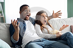 Excited interracial couple watching TV on couch at home