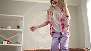 Excited joyful little girl jumping indoors laughing out loud. portrait of blond Caucasian child with long hair having