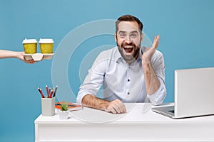 Excited joyful man work at desk with pc laptop isolated on blue background. Food products delivery courier service from