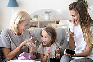 Excited kid girl holding lipstick doing makeup with mom grandma