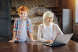 Excited kid joining his grandmother working on laptop