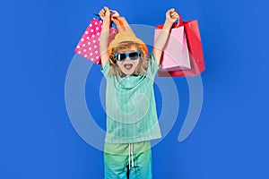 Excited kid with many shopping bags in studio. Funny amazed little boy in summer fashion kids clothes with shopping bags