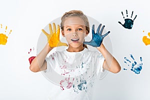 excited kid with paint on hands near hand prints on white.