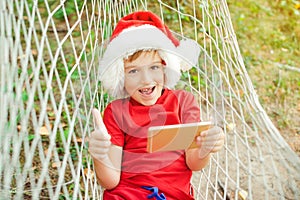 Excited kid playing games on smartphone and shows gesture like. Happy christmas holidays. Boy resting at hammock during family