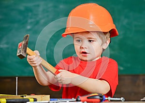 Excited kid playing with heavy hammer. Cute boy in orange helmet helping in workshop. Future profession concept