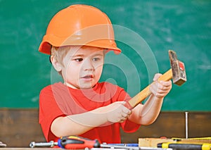 Excited kid playing with heavy hammer. Cute boy in orange helmet helping in workshop. Future profession concept