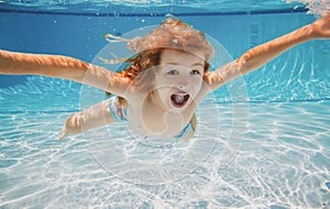 Excited kid swim underwater in pool. Child under water. Funny face portrait of child boy swimming and diving underwater