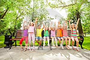 Excited kids with arms and sit in row on bench