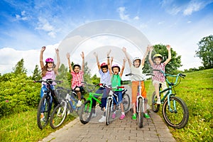 Excited kids in helmets on bikes with hands up