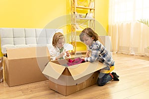 Excited kids laughing playing in new home carrying boxes, happy family with children enjoying relocation, small girl and