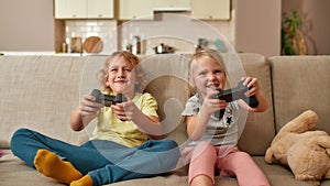 Excited kids, little boy and girl playing video games using joystick or controller while sitting together on sofa at