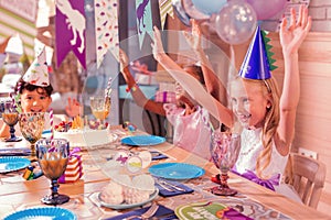 Excited kids putting hands up and dancing at the table