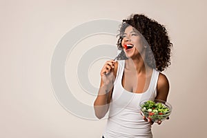 Excited lady eating healthy salad over light background