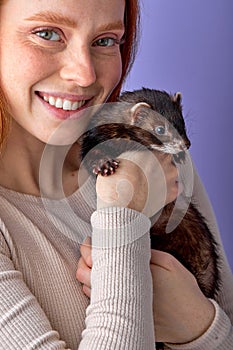 excited lady posing with ferret isolated in studio on purple background, cute domestic animal