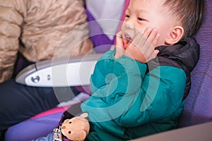 Excited little Asian  2 -3 year old toddler boy  wearing & fasten seat belts with teddy bear stuffed toy friend during flight on
