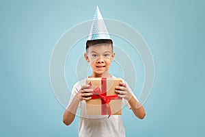 Excited little asian birthday boy wearing party hat holding wrapped gift box