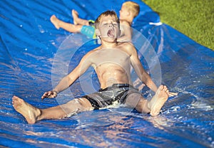 Excited little boys playing on a slip and slide outdoors