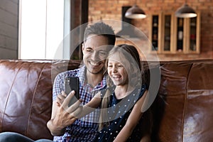 Excited little daughter girl and happy dad sitting on sofa