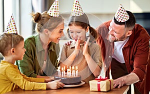 Excited little girl looking at cake and making wish while celebrating Birthday with family at home