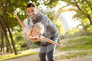 Excited little girl playing with her happy middle aged father in the park, child stretching hands, pretending to fly