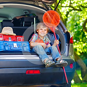 Excited little kid boy sitting in car trunk just before leaving for summer vacation with his family. Happy child with