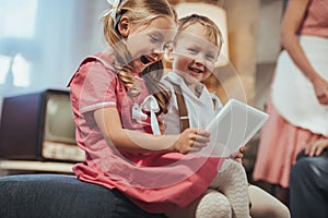 excited little kids in 1950s style clothes using digital tablet