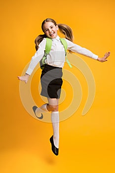 Excited Little Schoolgirl Jumping Over Yellow Studio Background.