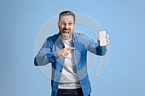 Excited male entrepreneur screaming and pointing at blank smart phone screen over blue background